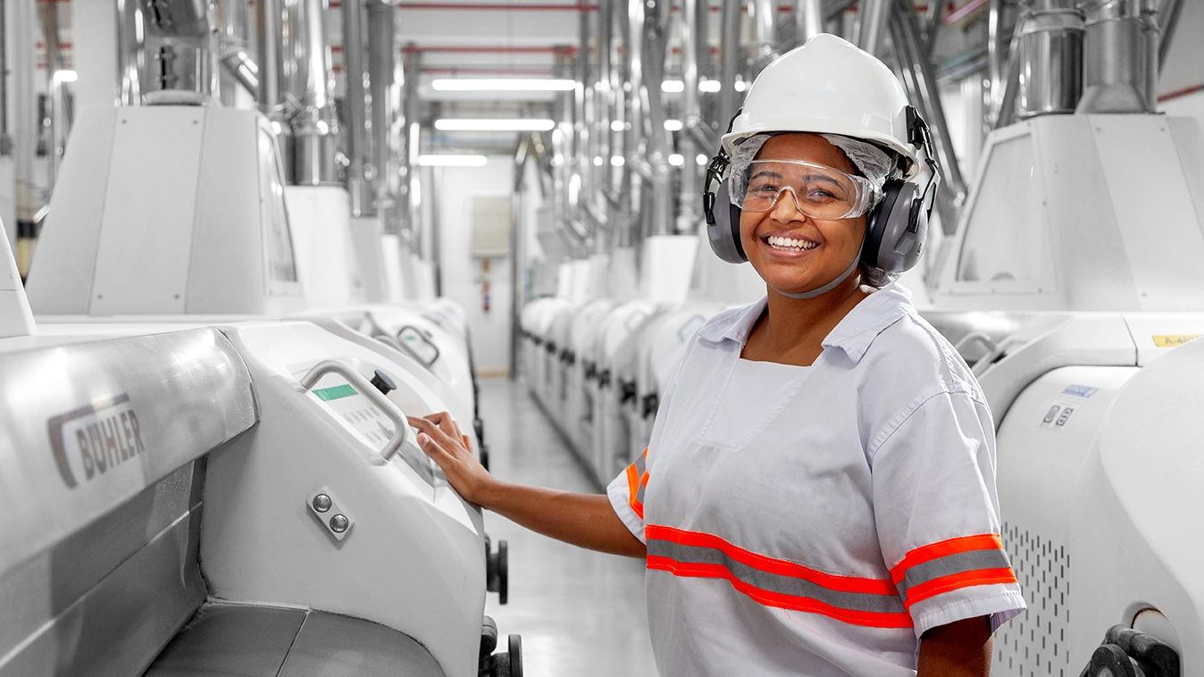 Fotografia industrial — operadora na linha de produção de soja — Operadora com capacete, óculos e protetor auricular no painel de controle da linha, na unidade da Bunge em Luís Eduardo Magalhães, Bahia.