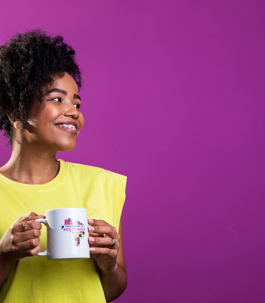 Fotografia institucional — colaboradora no escritório da Tenda — Colaboradora de camisa amarela em fundo roxo, segurando uma caneca, no escritório da Tenda Construtora. Uso institucional.
