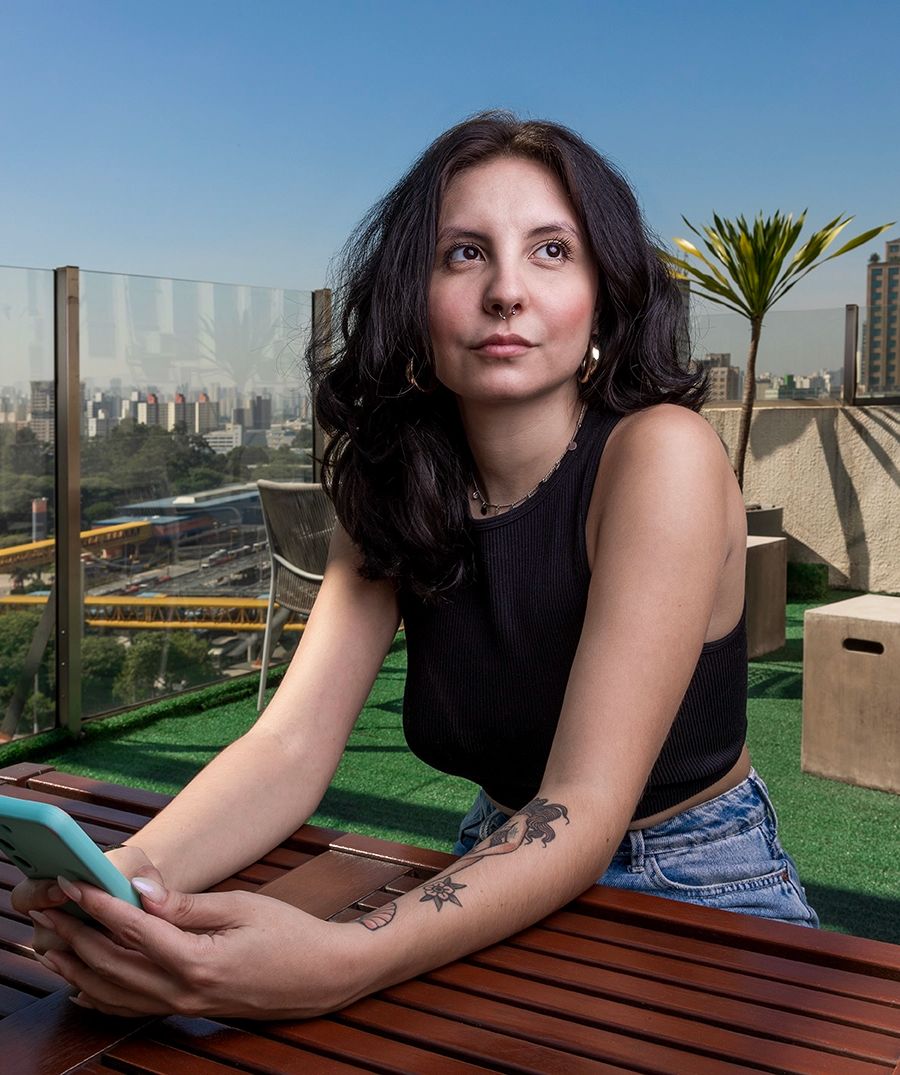 Fotografia institucional — colaboradora à mesa no escritório da Tenda — Colaboradora sentada à mesa com o celular, no escritório da Tenda Construtora. Uso institucional.