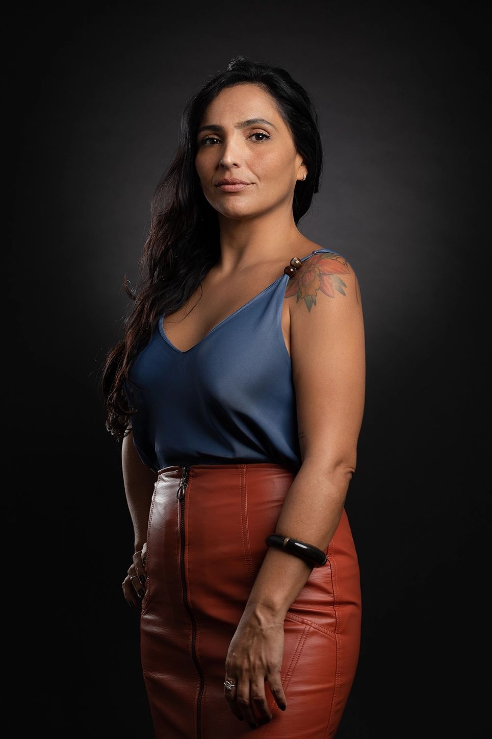 Retrato corporativo feminino em estúdio — Executiva de regata azul e saia de couro marrom, em estúdio no Alto da Lapa, São Paulo. Luz suave que desenha o maxilar, feito para posicionamento no LinkedIn.