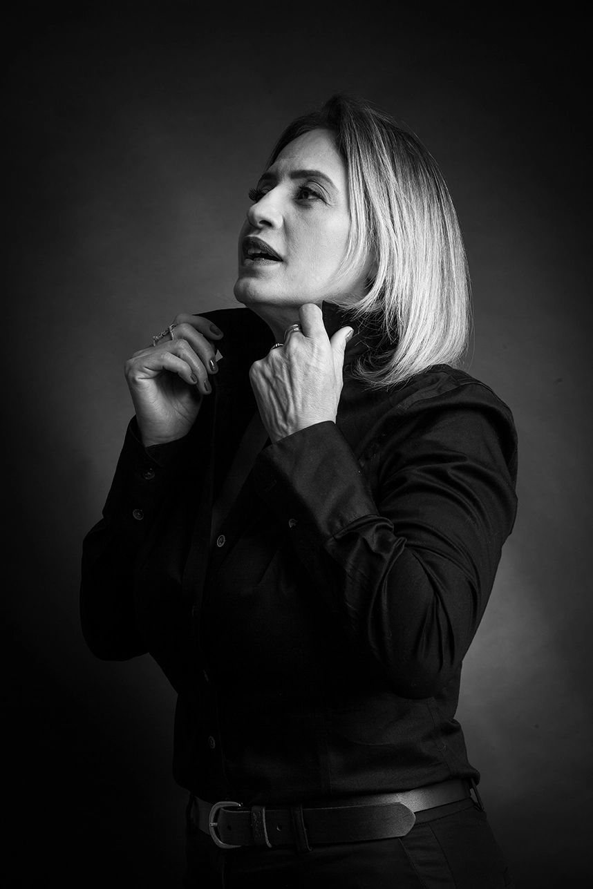 Retrato feminino em preto e branco — Executiva de camisa preta em fundo preto, em preto e branco, em estúdio no Alto da Lapa, São Paulo. Luz suave, feito para posicionamento no LinkedIn.